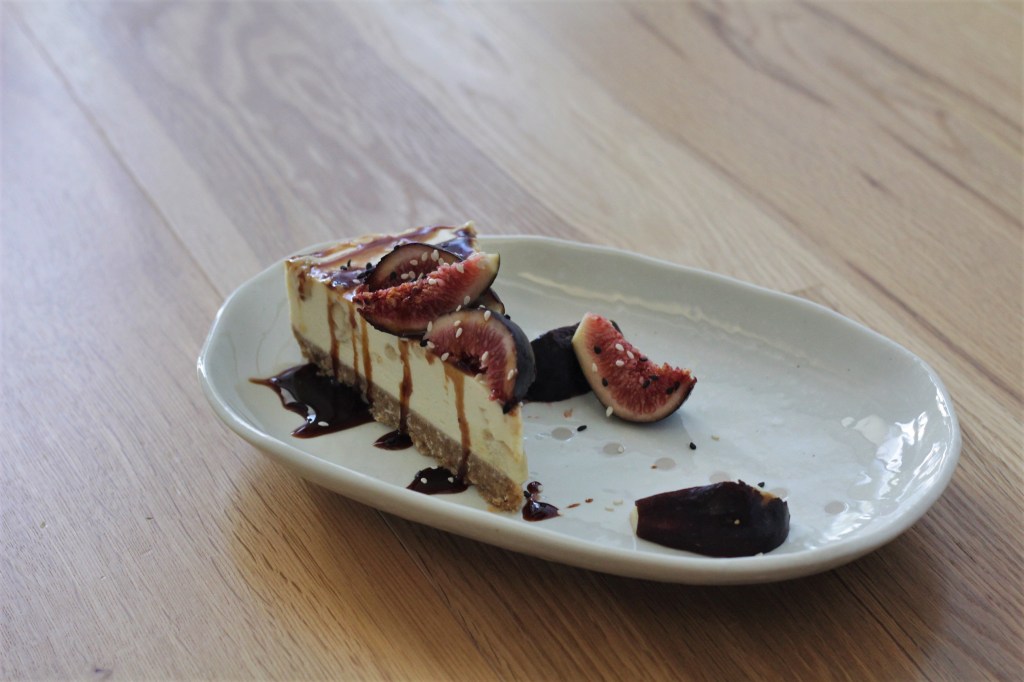 Picture shows a wedge-shaped slice of cream-coloured cheesecake with cut fresh figs and dark date syrup.