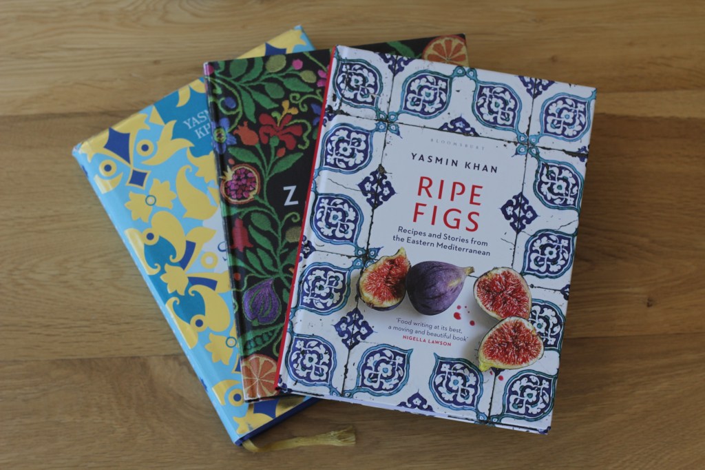 A stack of vibrant decorated cookbook covers fanned out. The top book is white with an elaborate blue tile pattern, photos of cut figs, and the title 'Ripe Figs' Yasmin Khan.