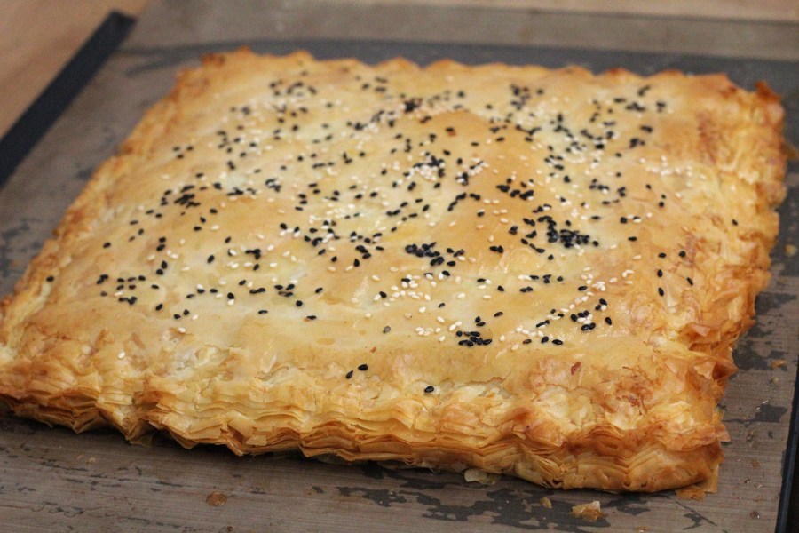 A golden pie with flaky edges and black and white sesame seeds on top.