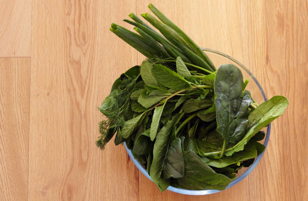A bowl full of trimmed spinach, herbs and spring onion.