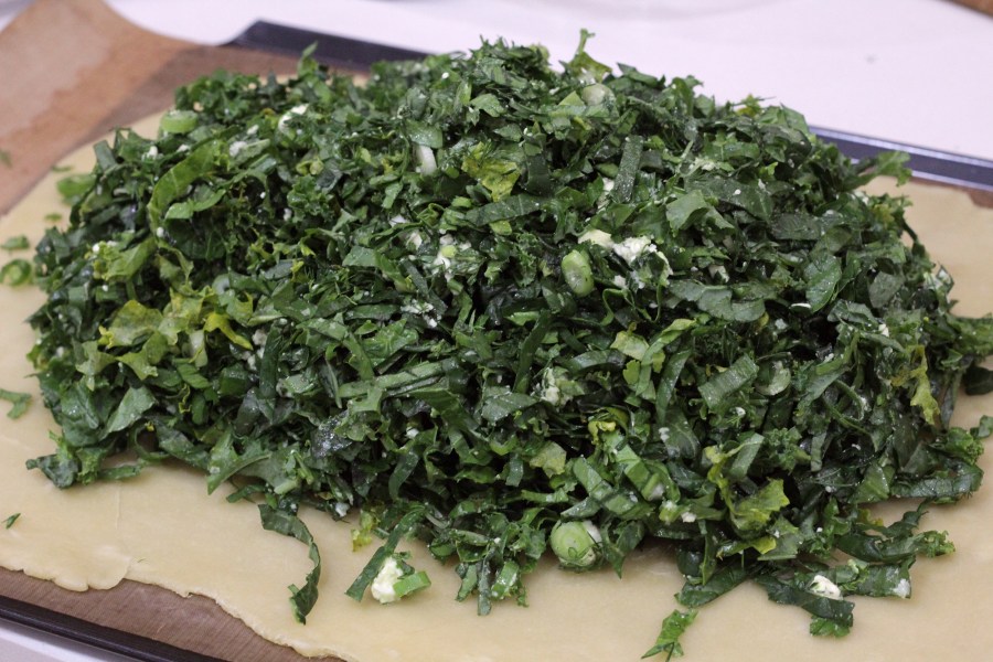 Image shows a sheet of homemade rough pastry with a pile of greens and cheese filling.